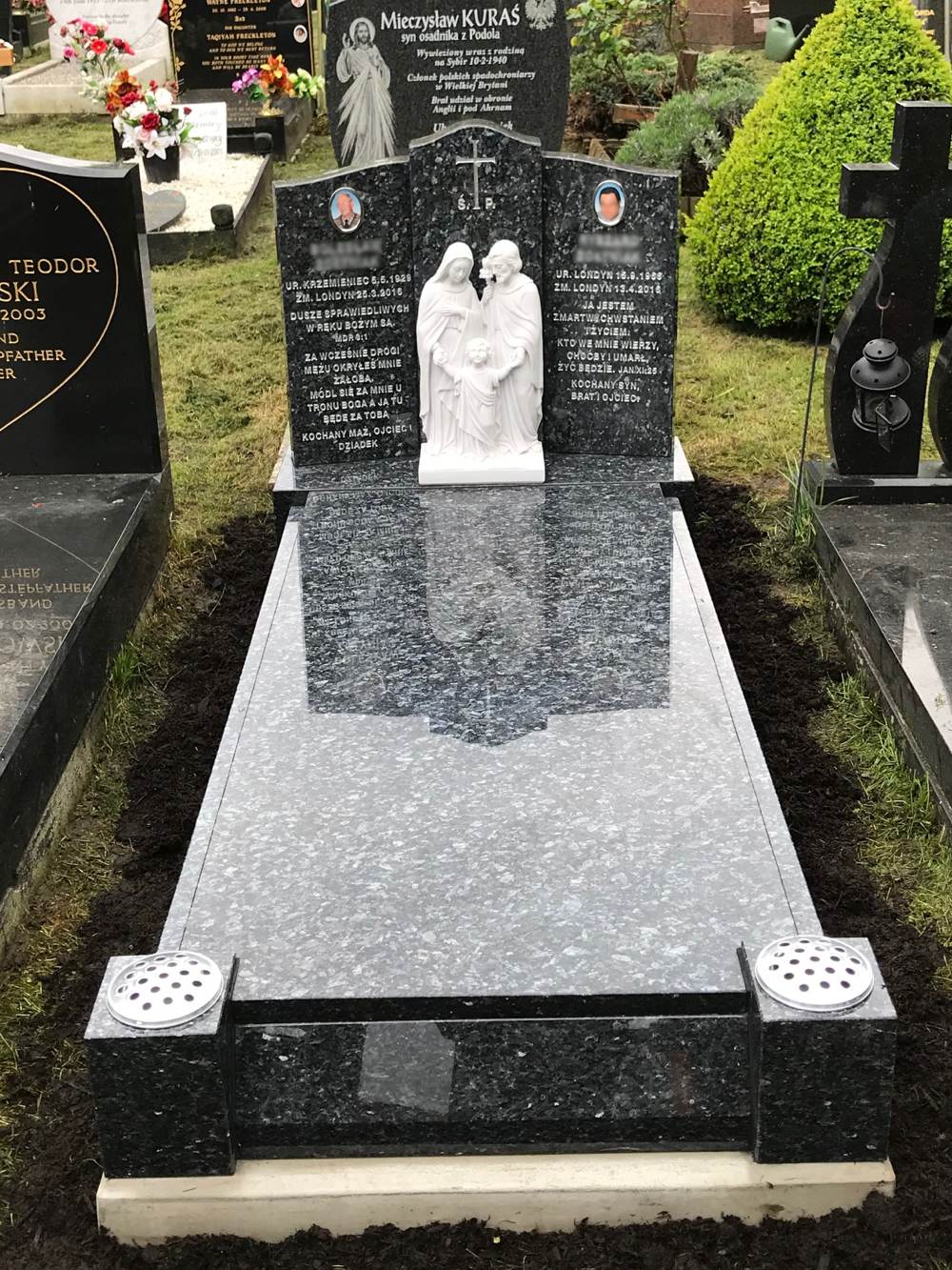 Blue Pearl Granite winged memorial with Statue of The Holy Family upon kerb set with centre cover slab and splayed foot kerb.