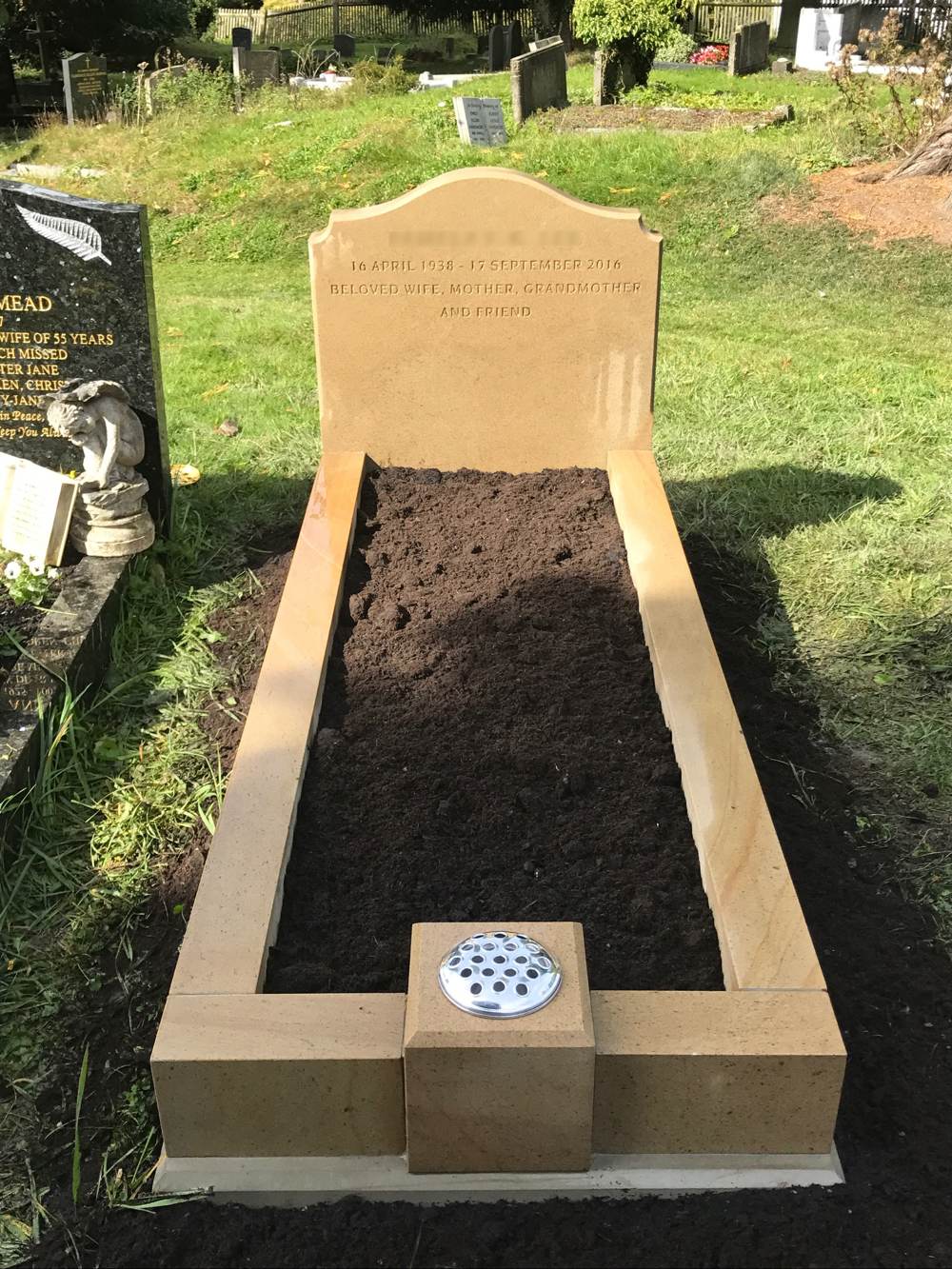 York stone round top scotia shoulders headstone upon kerb set with single vase foot post.
