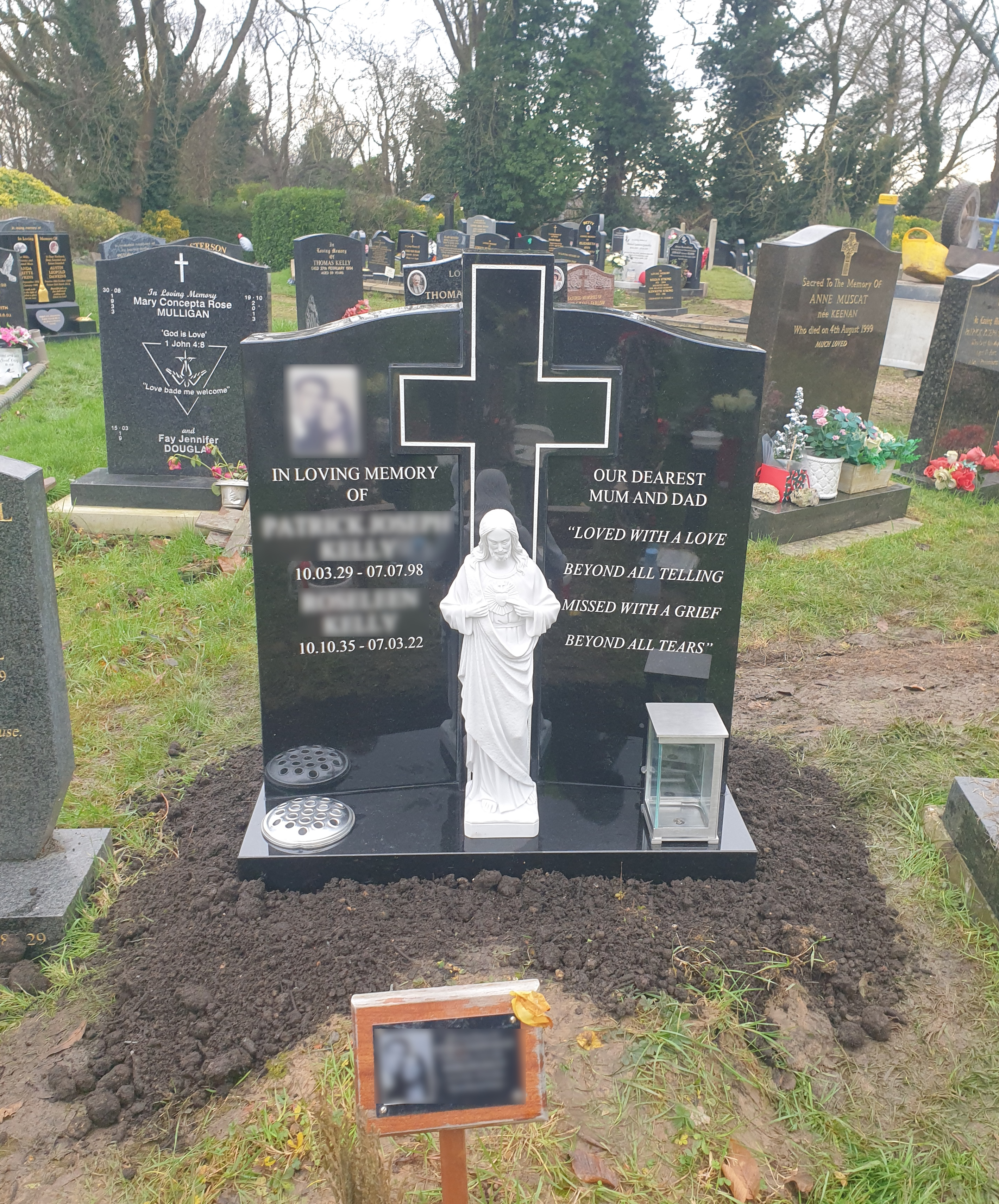 Black granite gates of Heaven style lawn memorial with central cut out cross and Sacred Heart Jesus statue.