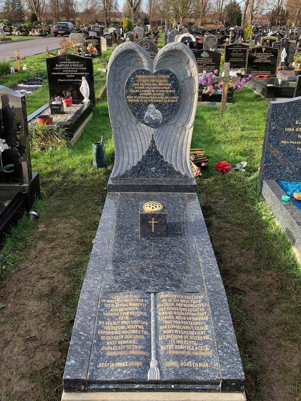 Blue Pearl full memorial with carved wings around heart, cover slab and book foot panel with carved cord and tassel and square vase on cover slab.