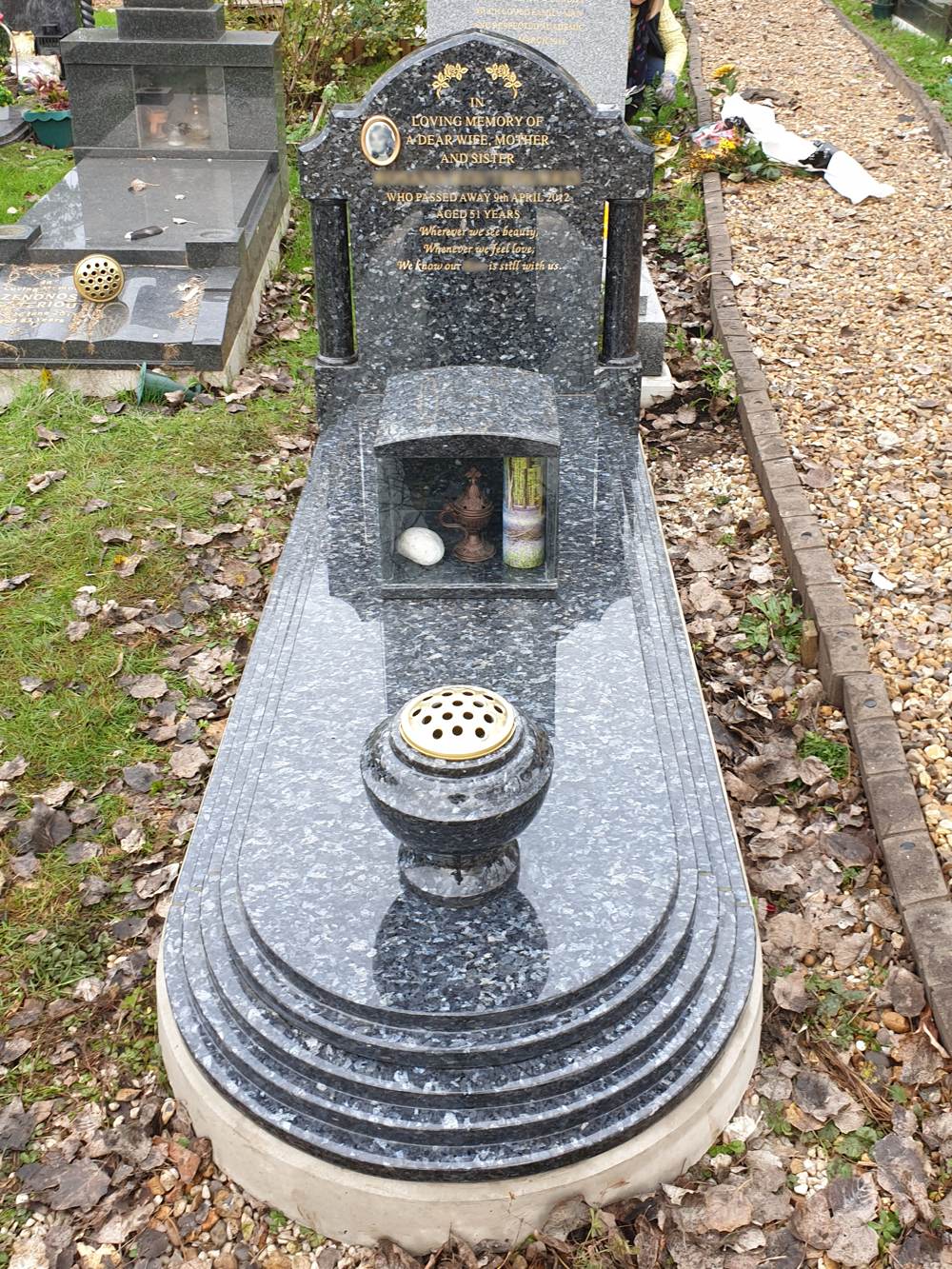 Blue Pearl Granite full memorial with classic shape headstone with turned and polished side columns upon rising step edged kerb set with cover slab and turned vase and candle box.